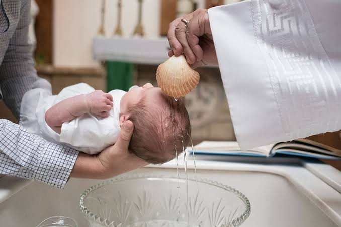 Sacerdote bautizando a un bebé con agua y concha en la pila bautismal